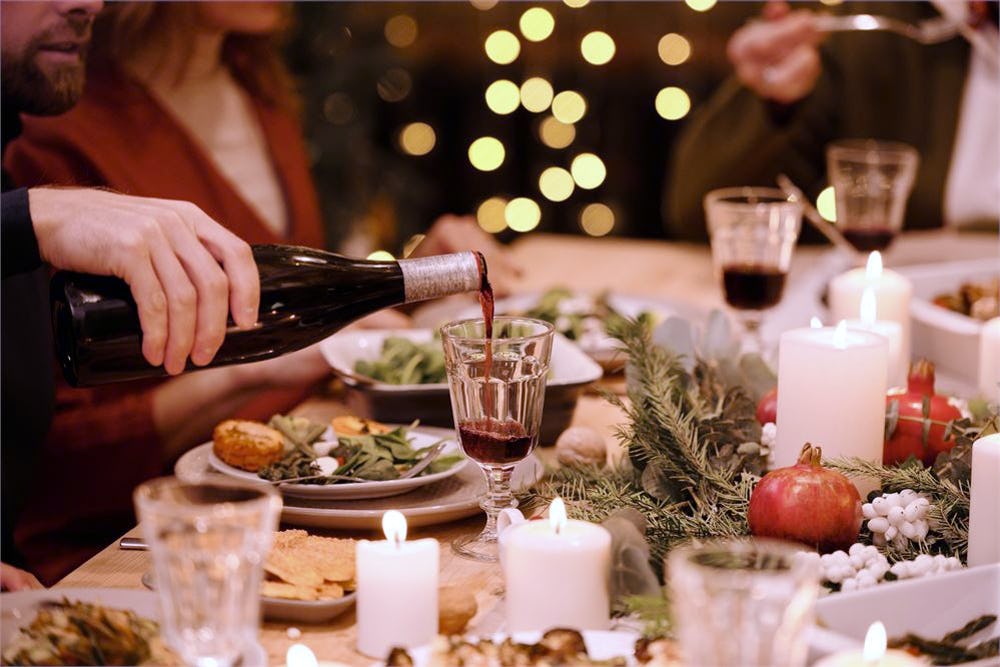 Image of wine being poured into a class on a Christmas table set with pomegranates and candles.